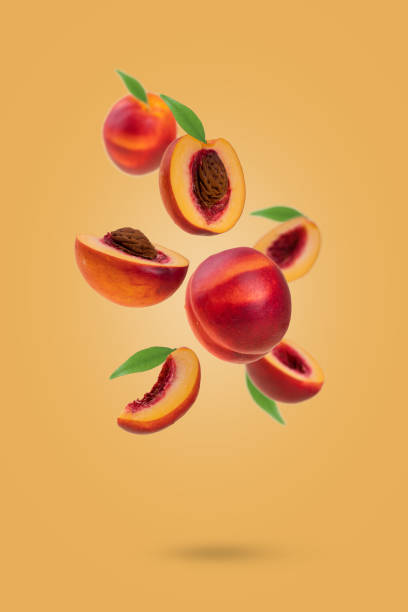 Flying fresh ripe nectarines - peaches with green leaves levitating  against yellow background.