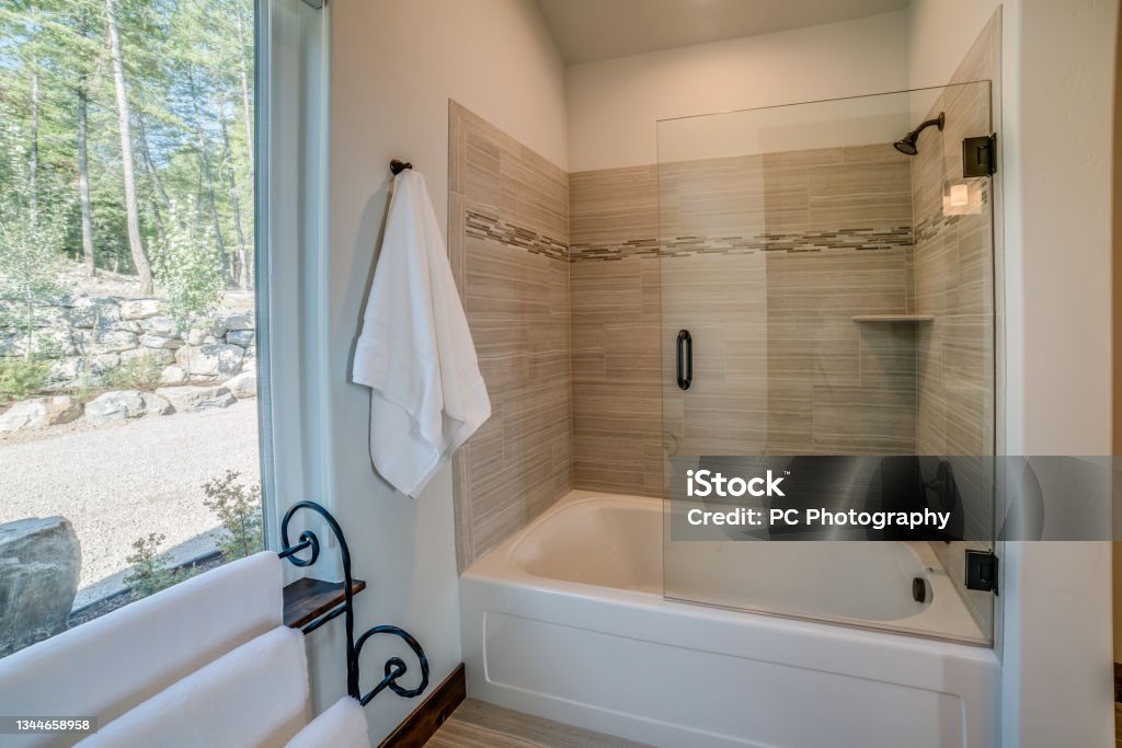 Half glass on tub shower combo White towels and large window give a light feel to this bathroom Bathtub Stock Photo