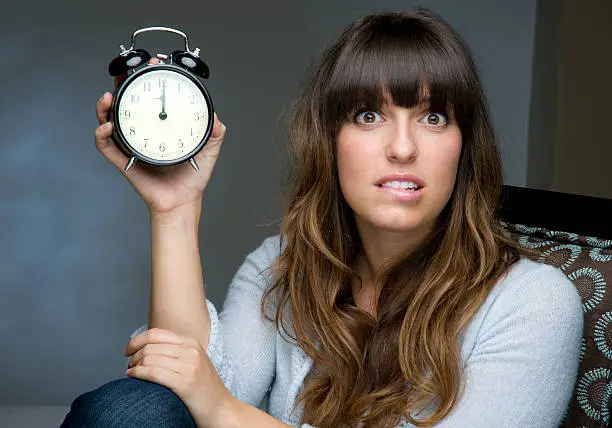 Woman holding a clock looking worried.