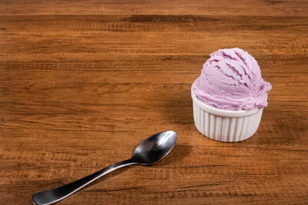 Photo of Grape-flavored purple ice cream served in the pot. A ball of ice cream accompanied by a spoon. Diagonally aligned elements with upper left space for free text.