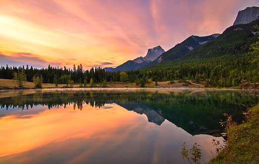 A colourful sunrise sky glowing over mountains and water at Quarry lake in the fall.