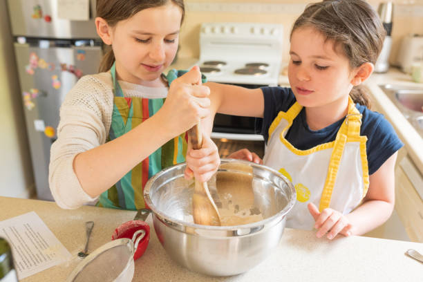 two girls working together to stir cupcakes mixture - mixing bowl imagens e fotografias de stock