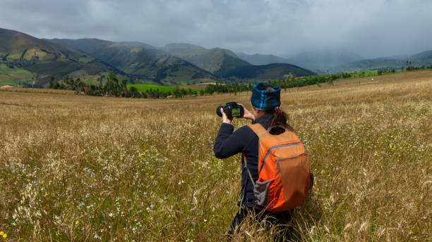 Close up of a beautiful Hispanic female scout seen from behind with a backpack taking a picture in the middle of a sown field on a cloudy morning
