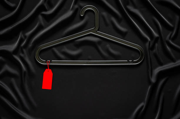 A black hanger with blank red price tag on black smooth and wavy cloth with space for text. Black Friday concept.