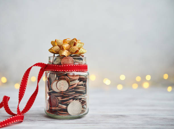 Holiday Savings Jar Filled with Coins and Christmas Ribbon and Bow Holiday Savings Jar Filled with Coins and Christmas Ribbon and Bow ira gold funds stock pictures, royalty-free photos & images