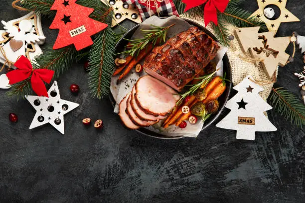 Christmas composition with baked ham on dark background. Traditional food concept. Top view, flat lay, copy space