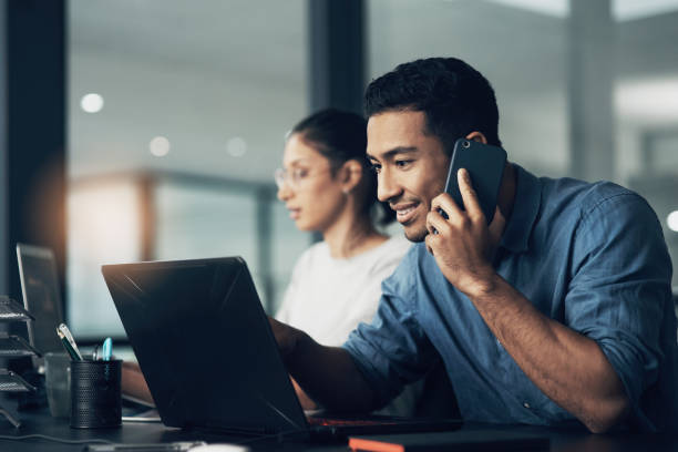 istock Shot of a young man using his cellphone while working on a laptop in a modern office 1344688168