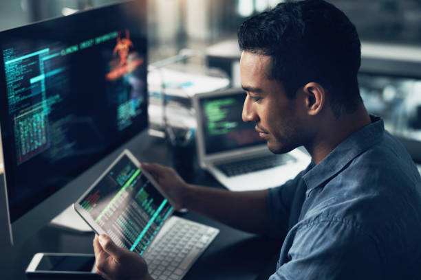 aufnahme eines jungen mannes mit seinem digitalen tablet und computer in einem modernen büro - cybersecurity stock-fotos und bilder