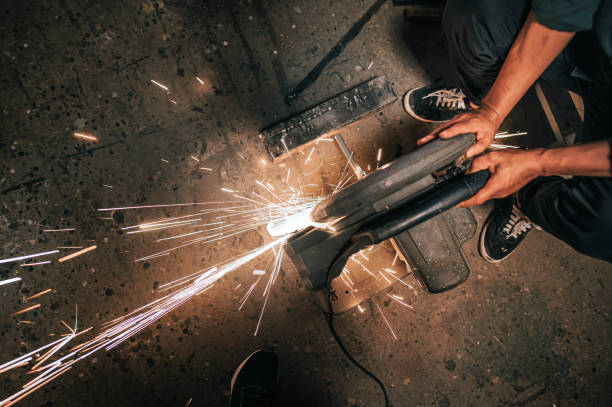 directly on top high angle view asian mature man welder grinding working in workshop welding cutting metal with grinder