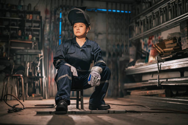 istock asian chinese female blue collar worker welder with protective workwear looking at camera with cool attitude in workshop garage sitting on stool 1344691973