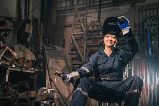 istock asian chinese female blue collar worker welder with protective workwear looking at camera smiling in workshop garage sitting on stool 1344691976
