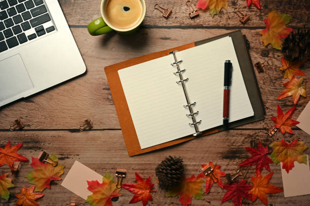 Computer laptop, empty notebook, coffee cup and autumn maple leaves on wooden table.