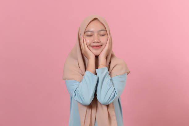 istock Charming hijab Asian girl with tender expression has rough cheeks keeps hands on cheeks dressed in hijab poses against pink background 1344694017