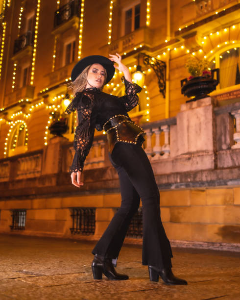 luci di natale in città, bella ragazza bionda vestita di nero con un cappello accanto a un edificio illuminato, stile di vita invernale - yoga winter urban scene outdoors foto e immagini stock