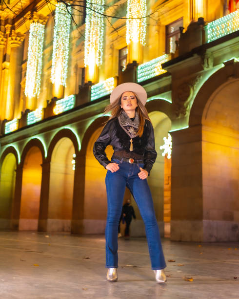 stile di vita invernale, ragazza bionda caucasica con jeans e giacca nera in città illuminata per natale di notte, in posa per la moda - yoga winter urban scene outdoors foto e immagini stock