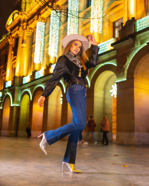 stile di vita invernale, ragazza bionda caucasica che indossa jeans e giacca nera in città illuminata per natale di notte, foto verticale - yoga winter urban scene outdoors foto e immagini stock