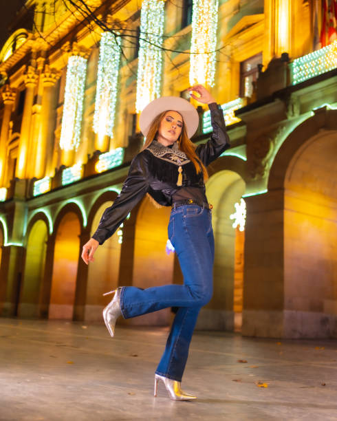 stile di vita invernale, giovane modella bionda caucasica che indossa jeans e una giacca nera in città illuminata per natale di notte - yoga winter urban scene outdoors foto e immagini stock