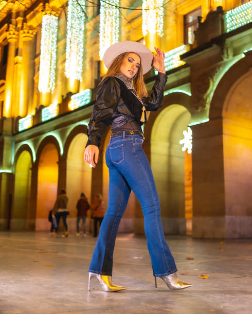 stile di vita invernale, giovane modella bionda caucasica che indossa jeans e una giacca nera in città illuminata per natale di notte - yoga winter urban scene outdoors foto e immagini stock