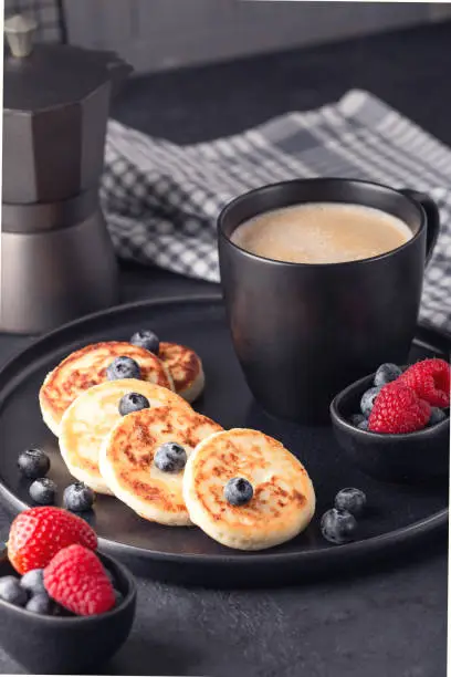 Close up of cheese pancakes with fresh berries on dark ceramic plate. Syrniki. Vertical photo - Image