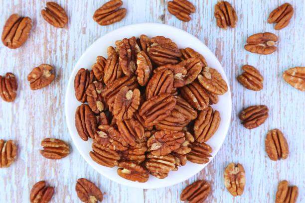 木の背景に散らばったいくつかのカーネルと乾燥ピーカンナッツのプレート - pecan nut hickory tree food and drink ストックフォトと画像