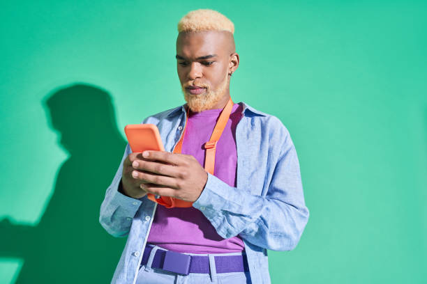 Multiracial gentleman holding his mobile phone and browsing something Choosing song. Horizontal view of young multiracial gentleman holding his mobile phone and browsing something. Isolated on green background black men with blonde hair stock pictures, royalty-free photos & images