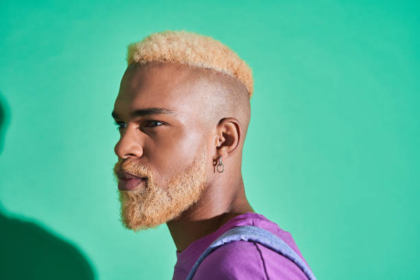 Multiracial man with blonde hair looking away while standing on green background Portrait of a serious handsome multiracial man with blonde hair looking away while standing on green background. People appearance concept black men with blonde hair stock pictures, royalty-free photos & images