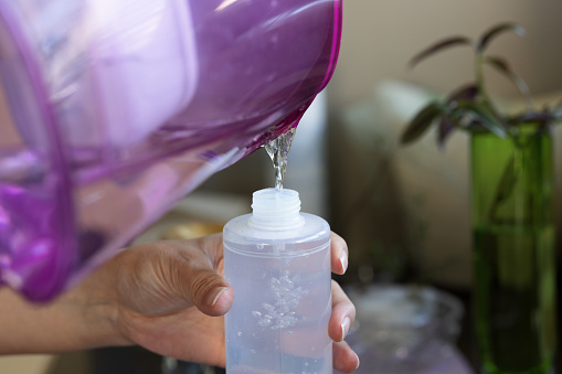 Plastic container being filled with water from a purple jug.