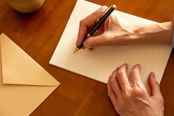 テーブルの上に置かれたひな形、封筒、ボールペン、コーヒー、ペンを持つ手 - message ストックフォトと画像