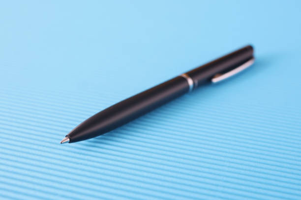 Black ballpoint pen lying on blue background closeup. Journalism concept