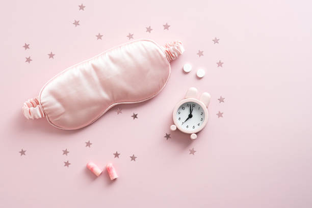 istock Flat lay sleeping mask, alarm clock, earplugs and pills on pink background. Accessories for sleep better at night 1344706336