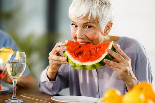 Mature woman biting fresh watermelon and looking at camera.