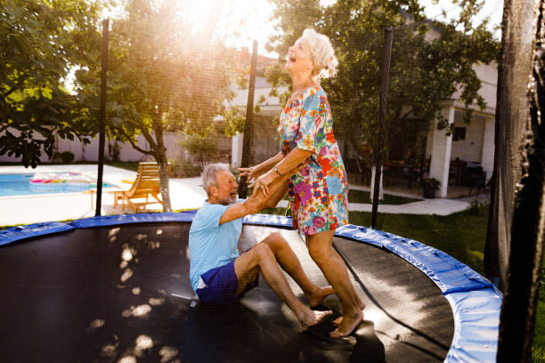 pareja de ancianos juguetona que se divierte en trampolín en el patio trasero. - action senior adult lifestyles couple fotografías e imágenes de stock