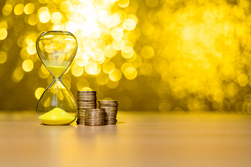 Hourglass and coins on shiny golden background.