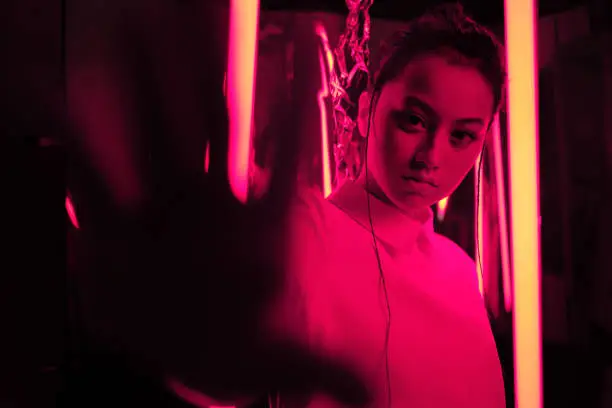 Portrait of young asian teenage girl with hand towards the camera, in red neon light. Cyber, futuristic portrait concept