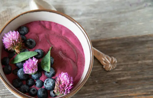 Healthy homemade snack or breakfast with organic greek yogurt blended with fresh blueberries and served with red clover blossoms isolated on wooden table from above