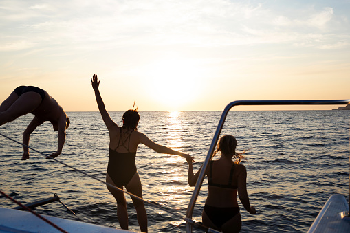 a group of friends jumping into the sea from a yacht at sunset.