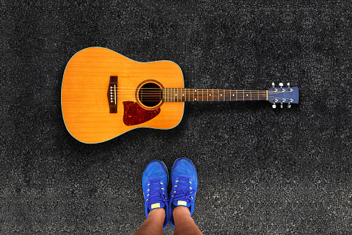 man legs in sneakers standing on road next to Acoustic guitar