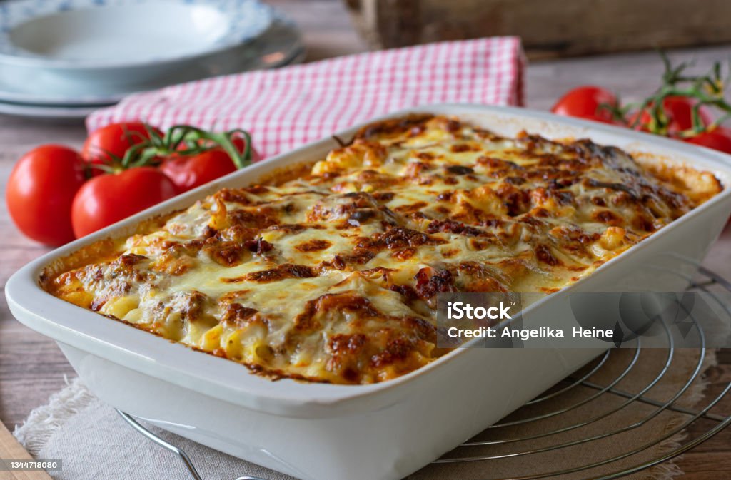 Pasta casserole with bolognese and bechamel sauce and mozzarella cheese topping Delicious homemade italian gratin dish with home cooked bolognese sauce and bechamel sauce topped with mozzarella cheese and served in a white baking dish on rustic table background. Closeup view Lasagna Stock Photo