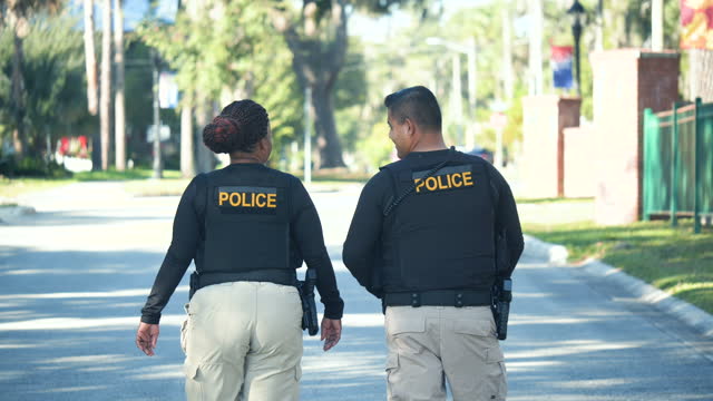 Two multiracial police officers walk on street, converse