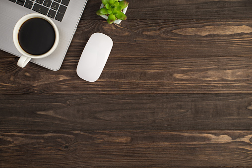 Top view photo of cup of coffee on laptop white mouse and plant on isolated dark wooden table background with empty space