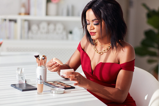 Beautiful African American Woman applying her makeup on with professional cosmetics products at home