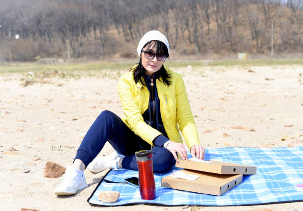 donna russa di 45 anni che va a mangiare la pizza mentre è seduta sulla spiaggia - russian ethnicity cold relaxation nature foto e immagini stock