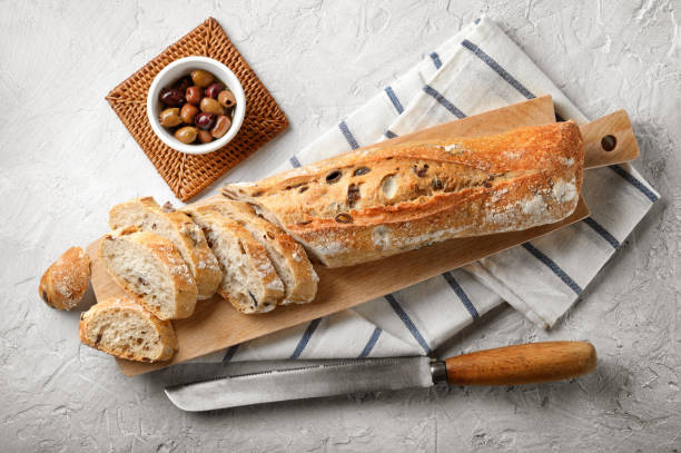 Taggiasca olive bread with cutting board and knife on white plaster background, Top view.