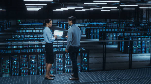 istock Data Center Female System Administrator and Male IT Specialist Talk, Use Laptop Computer. Information Technology Engineers work on Cyber Security Network Protection in Cloud Computing Server Farm. 1344731931