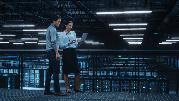 istock Data Center Female System Administrator and Male IT Specialist Talk, Use Laptop Computer. Information Technology Engineers work on Cyber Security Network Protection in Cloud Computing Server Farm. 1344731964