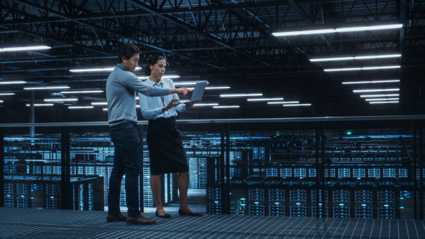 istock Data Center Female System Administrator and Male IT Specialist Talk, Use Laptop Computer. Information Technology Engineers work on Cyber Security Network Protection in Cloud Computing Server Farm. 1344731968