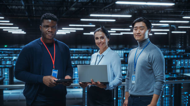 diversas equipes de administradores de sistemas de data center e especialistas em ti usam laptop e tablets, sorrindo na câmera. os engenheiros de ti trabalham na proteção de segurança cibernética na fazenda de servidores de computação em nuvem. - network server technology computer computer network - fotografias e filmes do acervo