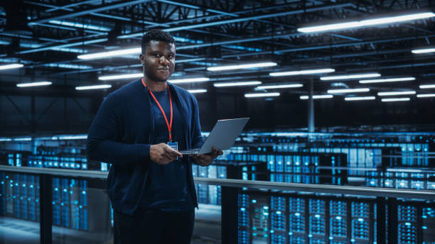 Portrait of a Data Center Engineer Using Laptop Computer. Server Room Specialist Facility with African American Male System Administrator Working with Data Protection Network for Cyber Security. Portrait of a Data Center Engineer Using Laptop Computer. Server Room Specialist Facility with African American Male System Administrator Working with Data Protection Network for Cyber Security. database photos stock pictures, royalty-free photos & images