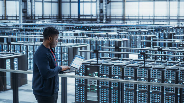 ingénieur de centre de données utilisant un ordinateur portable. installation de spécialiste de l’informatique en nuage de la ferme de serveurs avec un administrateur système masculin afro-américain travaillant avec le réseau de protection des donn - datacenter photos et images de collection