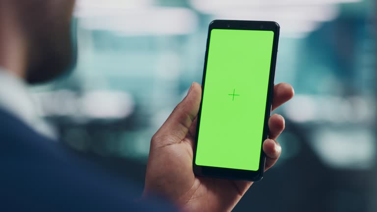 Black Man with Green Screen Chroma Key Smartphone in Office. African-American Person using Internet, Social Media, Online Shopping with Mobile Phone Device. Focus on Display, Hand